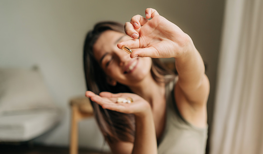 Mujer sonriente feliz sosteniendo una píldora omega en la mano. photo