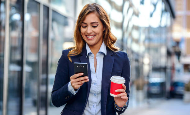 Businesswoman drinking coffee and using mobile phone in front of the office. Business, lifestyle concept stock photo