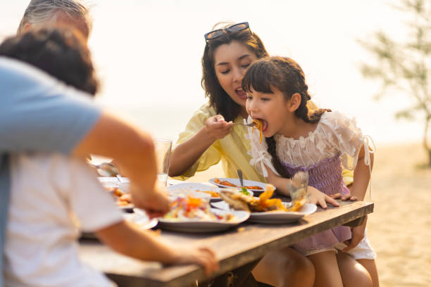 istock Multi-Generation Asian family having dinner together on the beach at summer sunset. 1487058898