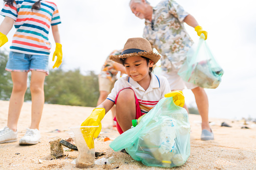 Group of Volunteers multi-Generation Asian family picking up plastic trash and garbage together at the beach on summer holiday vacation. Environmental conservation earth day and waste pollution concept.