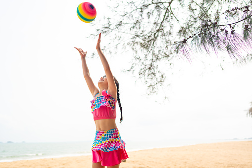 Happy Asian family travel ocean on summer holiday vacation. Little Asian child girl kid in swimsuit enjoy and fun outdoor activity lifestyle playing ball at tropical island beach in summer sunny day.
