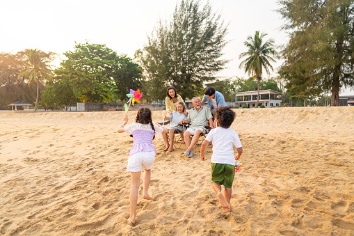 Group of Asian Multi-Generation family in casual clothing enjoy and fun outdoor lifestyle sitting and playing together at tropical island beach at sunset during travel ocean on summer holiday vacation