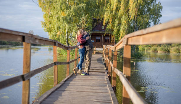 счастливая молодая влюбленная пара гуляет по мосту на закате. мужчина обнимает и собирается поцеловать чувственную женщину. - couple autumn embracing bridge стоковые фото и изображения