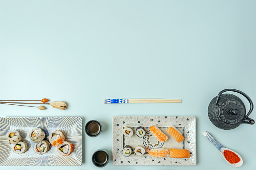 Sushi plates, teapot, soy sauce, chopsticks and empty space with light blue background