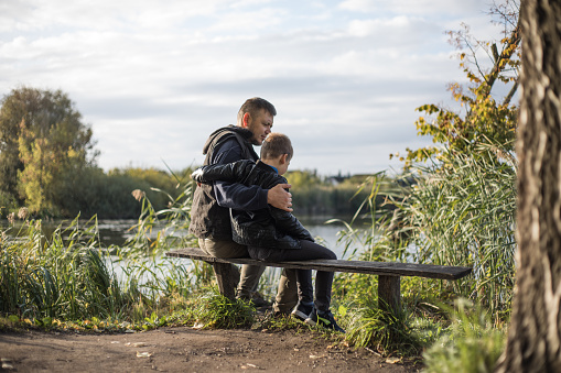 Father hugging his son outdoors on the bench. Precious moments between Dad  and son