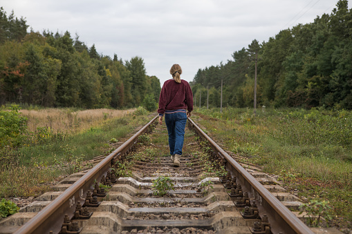A rear view of a young woman  walking away along the rails of a railway road. The concept of departure