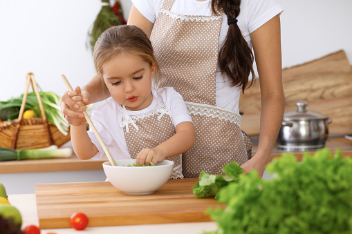 Mother and daughter playing and cooking holiday pie or cookies for Mother's day, casual lifestyle photo series in real life interior. Happy family in the kitchen