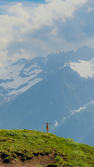 Silhouette of female in distance on top of the mountain hiking on green hill with background view of the beautiful snowcapped mountains peaks in Sunnmore Alps of Norway, Scandinavia