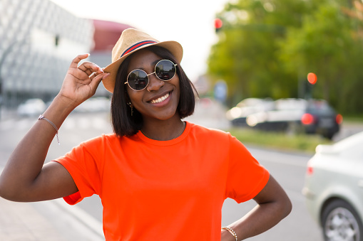 Young black woman tourist with orange t-shirt and sunglasses enjoying summer in the city, lifestyle photos