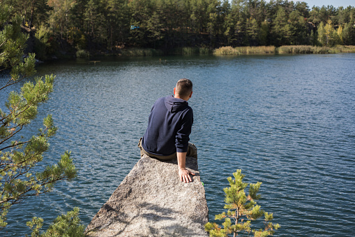Man sitting on rock enjoying the view over a forest lake a beautiful fall day