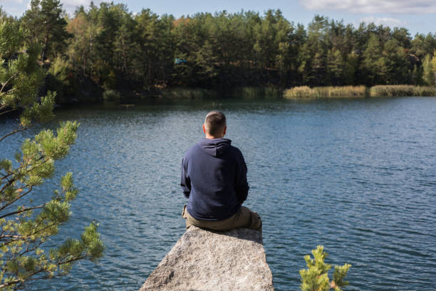 istock Man sitting on rock enjoying the view over a forest lake a beautiful fall day 1487063591