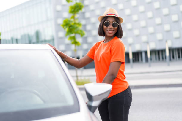 City life: black woman in orange shirt and sunglasses stepping into car