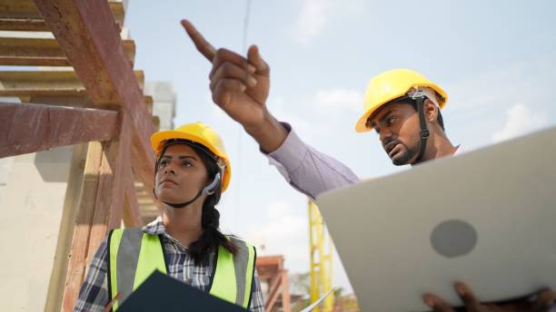 istock Professional civil engineer or building architect discussing with female foreman about house model in blueprint on laptop at housing project construction site. Team of contractor in safety uniform working in real estate business. building construction. 1487067651