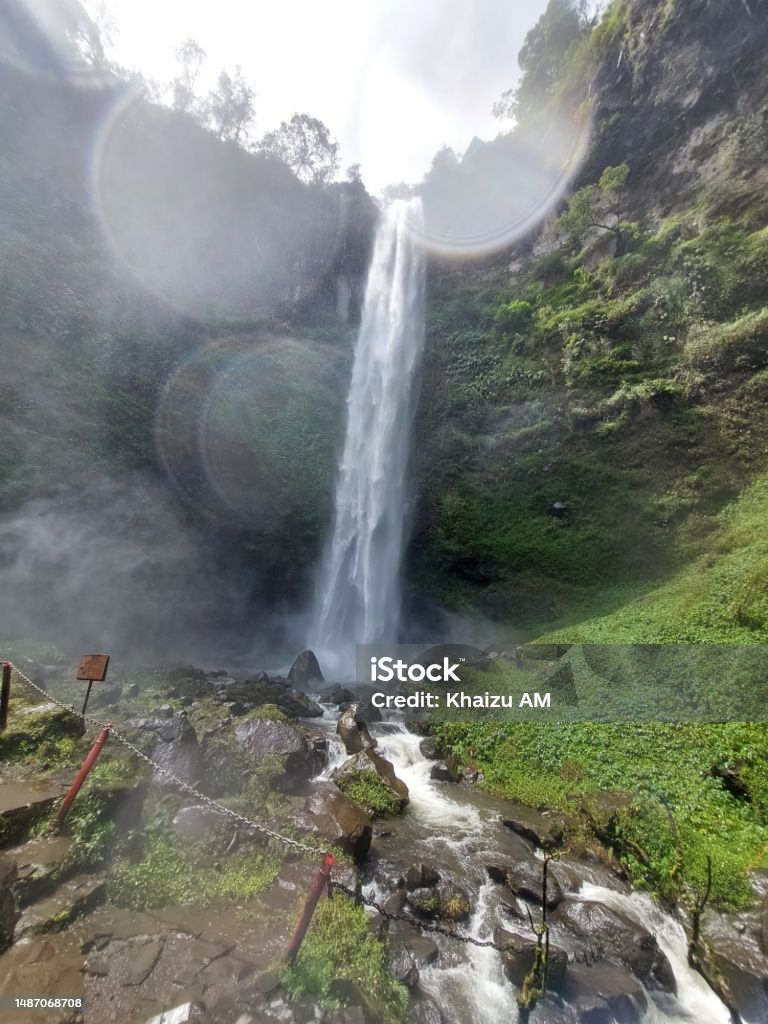 Stunning natural beauty at Coban Rondo Waterfall in Malang The photo shows a tall and swift waterfall against a backdrop of rocky cliffs and green trees.  This waterfall is named Coban Rondo which means widow waterfall.  This waterfall has a height of about 84 meters and is located at an altitude of 1,134 meters above sea level12.  This waterfall comes from a spring on the slopes of Mount Kawi Color Image Stock Photo