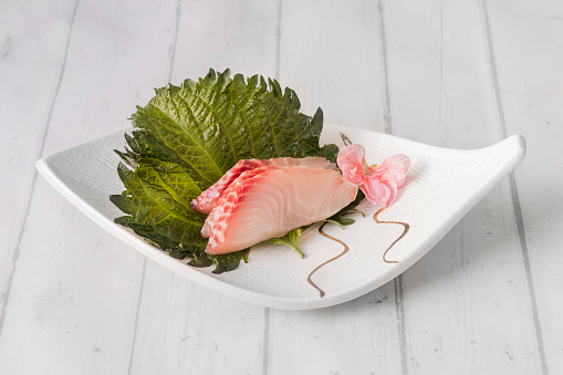 Pieces of sea bream sashimi on shiso leaf and white porcelain plate