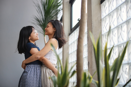 Love, care, and family bonding were on display as an Asian mom affectionately hugged her daughter by the living room window.
