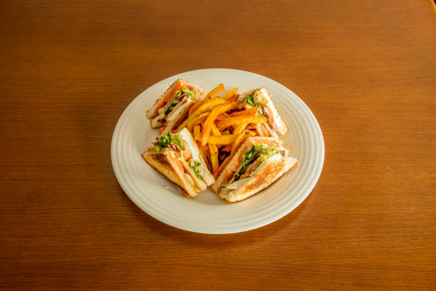 Club sandwich drizzled with mayonnaise sauce, fried chicken fillet, boiled egg, lettuce and tomato, fried bacon, crispy sliced bread and side of French fries.