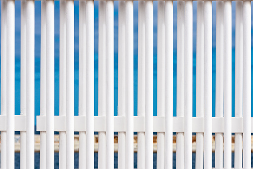 Bars of a white fence against the blue sky and the sea as abstract background