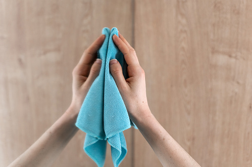Close-up view of hand with blue microfiber rag for cleaning mirror in bathroom. Woman holding cloth wiping glass surface at home. Housekeeping concepts