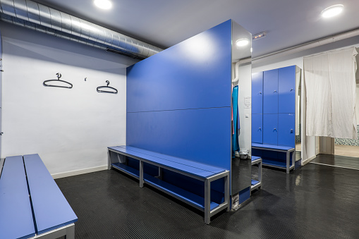 Blue wooden lockers with matching bench seats, mirrors and black hangers in a gym locker room