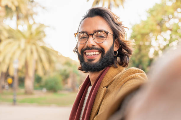 istock Attractive man with glasses and beard taking a selfie smiling outdoors in the park. 1487079477
