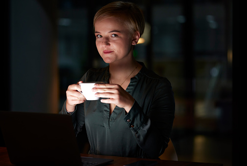 Coffee, smile and woman in dark office working late night,  commitment and vision with time management success. Happy businesswoman, overtime and relax on break from overtime work at startup business