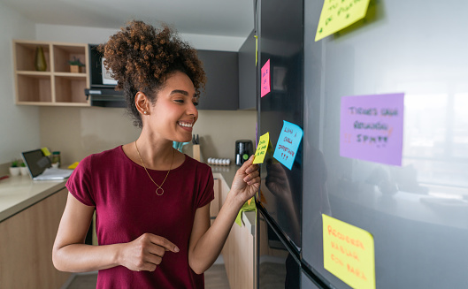 Happy African American woman at home planning her day using sticky notes on the fridge