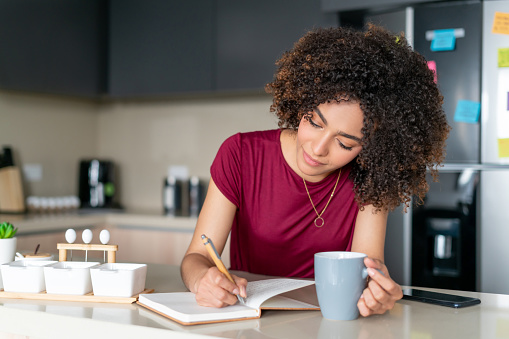 Happy African American young woman at home planning her day while drinking coffee