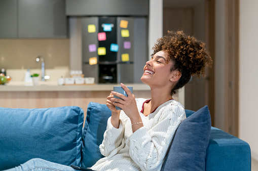 Happy African American young woman relaxing at home and drinking a cup of coffee