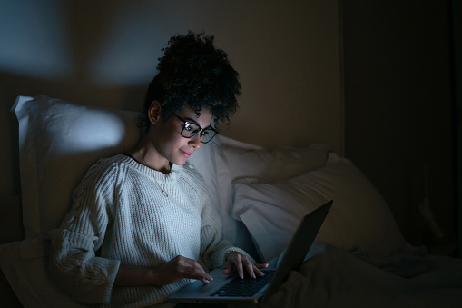 African American woman working late at a home in bed and using her laptop computer - lifestyle concepts