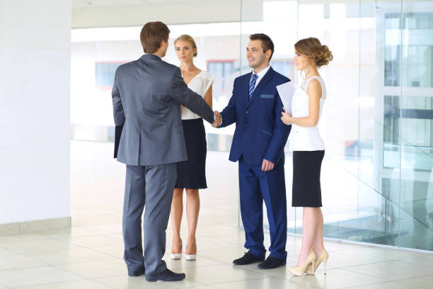 istock Two confident businessmen shaking hands and smiling while standing at office together with group of  colleagues 1487081591