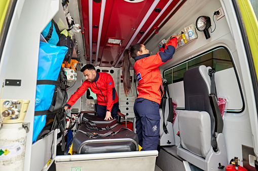 Man and woman in 20s and 30s wearing uniforms, standing inside ambulance, and organizing equipment.