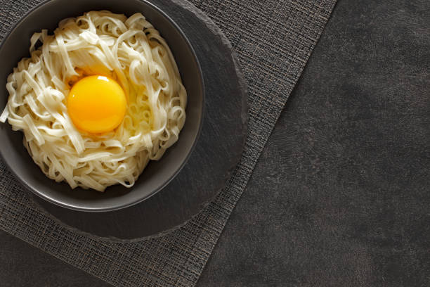 Flat udon noodles with raw egg, on slate stone plate round, dark background, top view