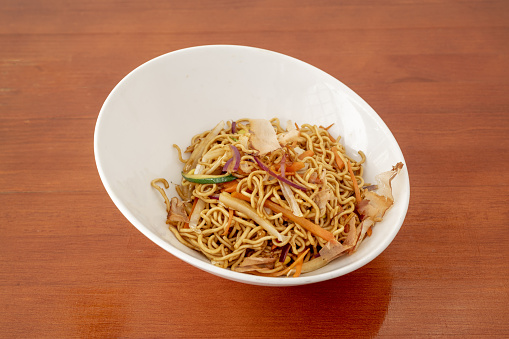 White bowl of sauteed noodles with fresh vegetables and yakisoba sauce on orange table