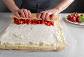 Making swiss roll. Get´s rolled up with whipped cream and strawberry filling by woman´s hands on kitchen counter.