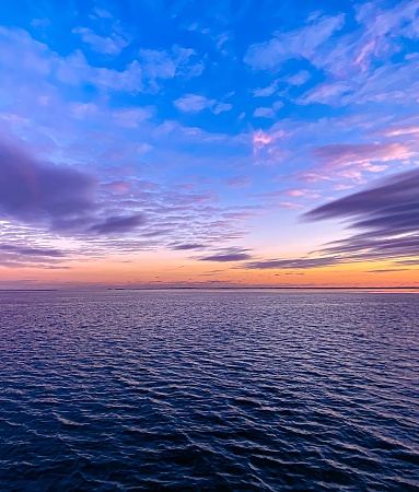 Sunset over bay, with dramatic sky and slightly choppy water, orange, purple, and blue hues in sky, majestic mood. Saturated colors. Copy space.