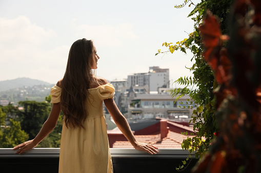 Young woman standing on balcony, back view. Space for text