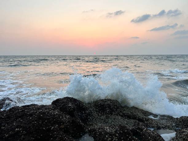 istock a wave crashes onto the rocks on the beach at sunset 1487091250