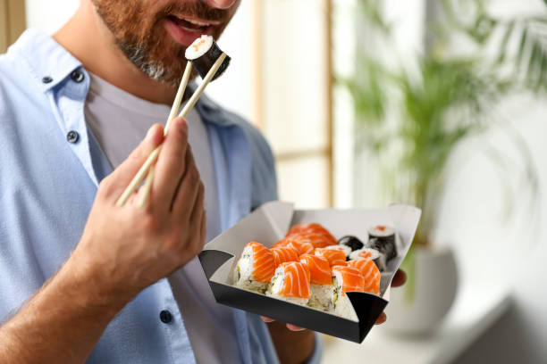 istock Handsome man eating sushi rolls with chopsticks indoors, closeup 1487091706