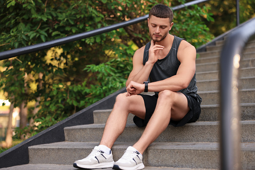 Attractive serious man checking pulse after training on stairs in park