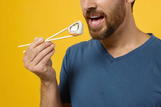 istock Man eating sushi roll with chopsticks on orange background, closeup 1487093688