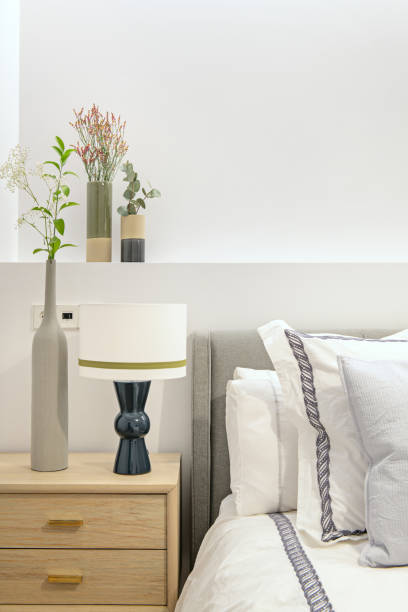 istock Fabric upholstered bedroom headboard attached to plasterboard construction with vases of flowers and light wood nightstand with blue lamp and lots of cushions on mattress 1487096407