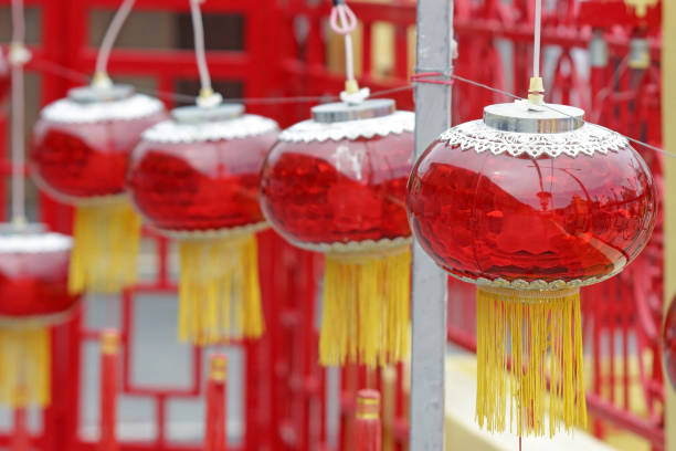 A row of decorative red Chinese glass lanterns with gold tassles. Electric outdoor lights for deoration at a Chinese Buddhist temple in southeast Asia. Daytime, no people.