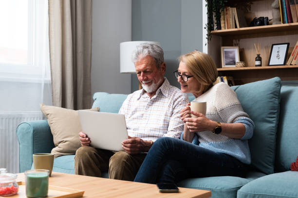 istock Happy middle aged family couple relaxing on sofa, using computer web surfing information shopping together at home. Elderly man showing laptop apps to retired wife, older generation with tech concept. 1487098047