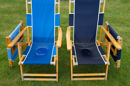 Pair of soaked canvas deckchairs seen in a stately home park. The seats can be seen, filled with water after a heavy downpour.