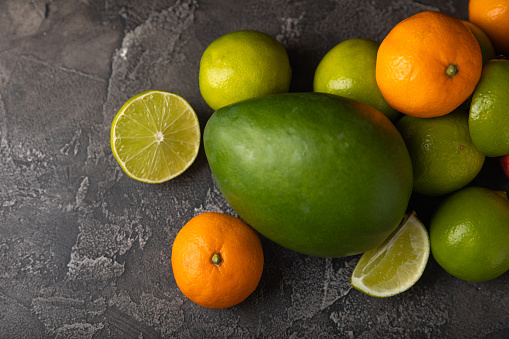 Fresh, bright exotic fruits on a dark marble background.Lime, tangerine and mango.Top view.Copy space.