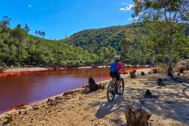 woman cycling with electric mountain bike at red river Rio Tinto, Andalusia, Spain nice woman with electric mountain bike on a bike tour along river Rio Tinto with its natural red water in Andalusia, Spain via verde spain stock pictures, royalty-free photos & images