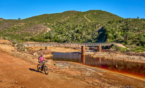 woman cycling with electric mountain bike at red river Rio Tinto, Andalusia, Spain nice woman with electric mountain bike on a bike tour along river Rio Tinto with its natural red water in Andalusia, Spain via verde spain stock pictures, royalty-free photos & images