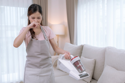 Young Asian woman spending her free time on vacation cleaning the living room at home, She had a stuffy nose and sneezing from allergic to dust.