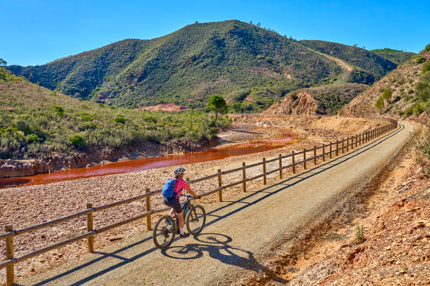 woman cycling with electric mountain bike at red river Rio Tinto, Andalusia, Spain nice woman with electric mountain bike on a bike tour along river Rio Tinto with its natural red water in Andalusia, Spain via verde spain stock pictures, royalty-free photos & images